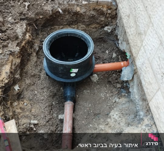 צינור ביוב כתום מחובר למיכל שחור באדמה